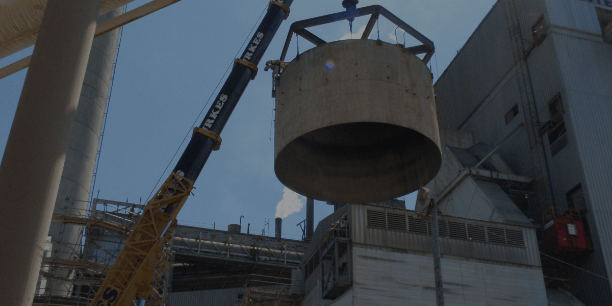 Burkes crane lifting large concrete tank section during demolition project at an industrial facility.