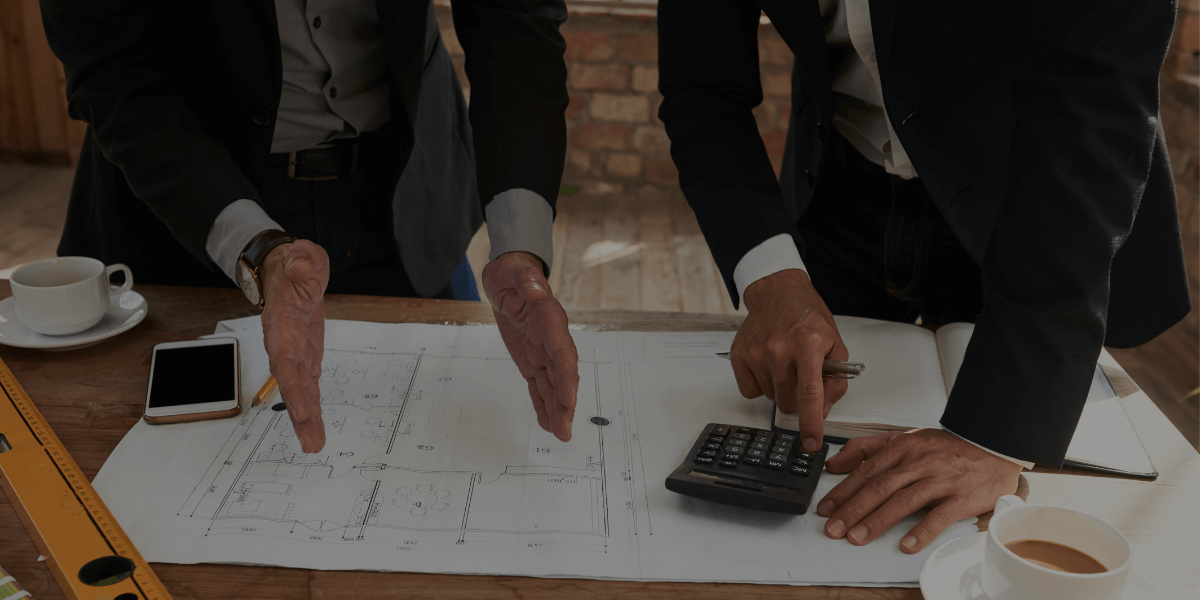 Two professionals reviewing industrial electrical project plans on a blueprint with calculator and measuring tools.