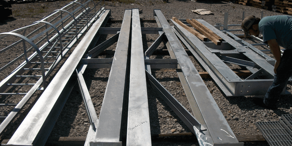 Fabricated structural steel components and ladder assemblies laid out at a job site for industrial construction installation.