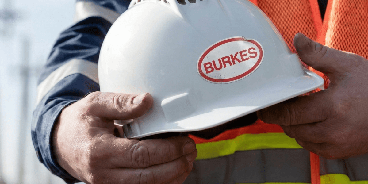 Burkes Mechanical worker holding a white hard hat with the Burkes logo while wearing high-visibility safety gear, representing the company’s strong safety culture and commitment to zero OSHA citations in industrial construction, fabrication, and mechanical services.