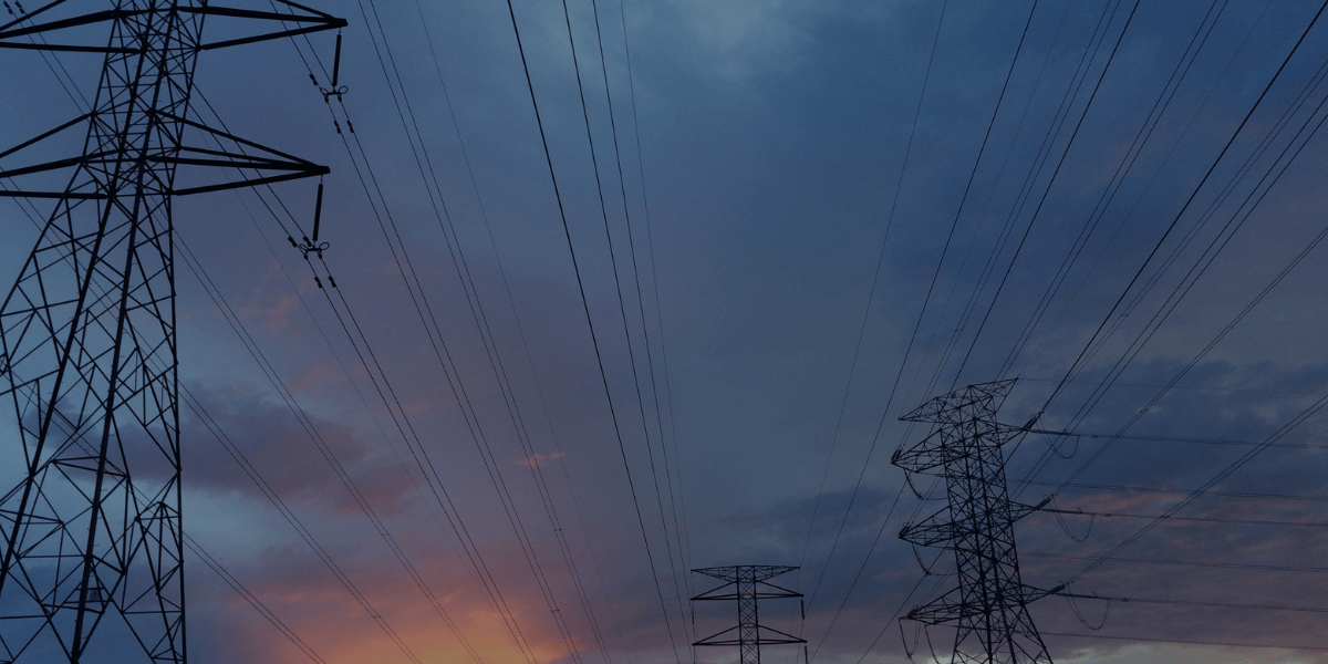 High-voltage transmission towers and power lines at sunset, representing industrial power distribution.