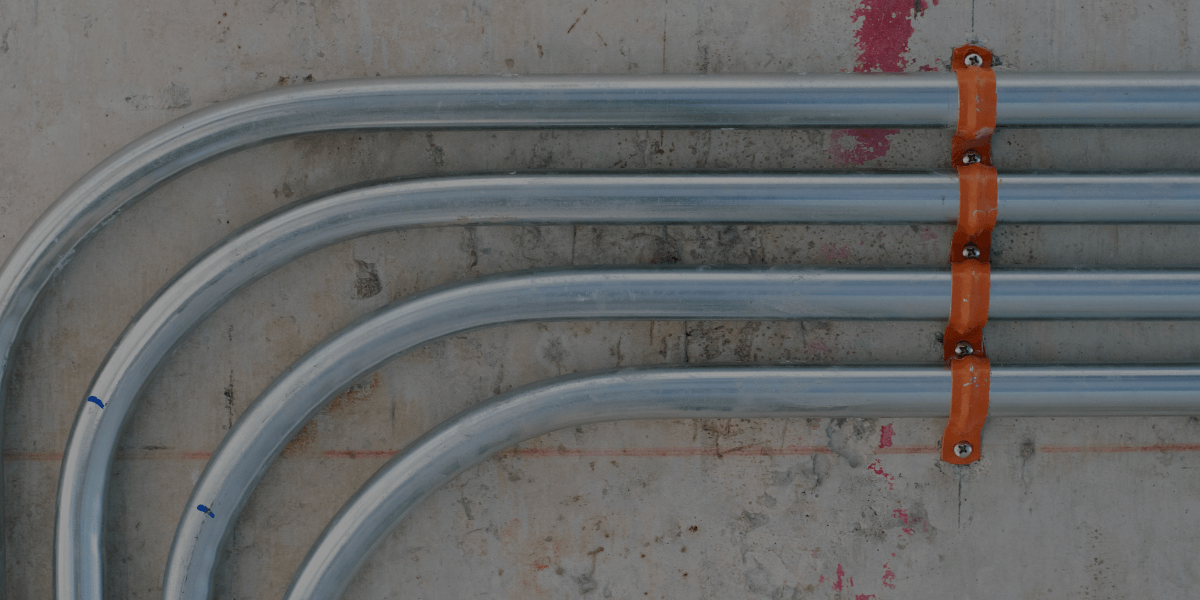 Electrical conduit installation with multiple bends secured to a concrete wall.