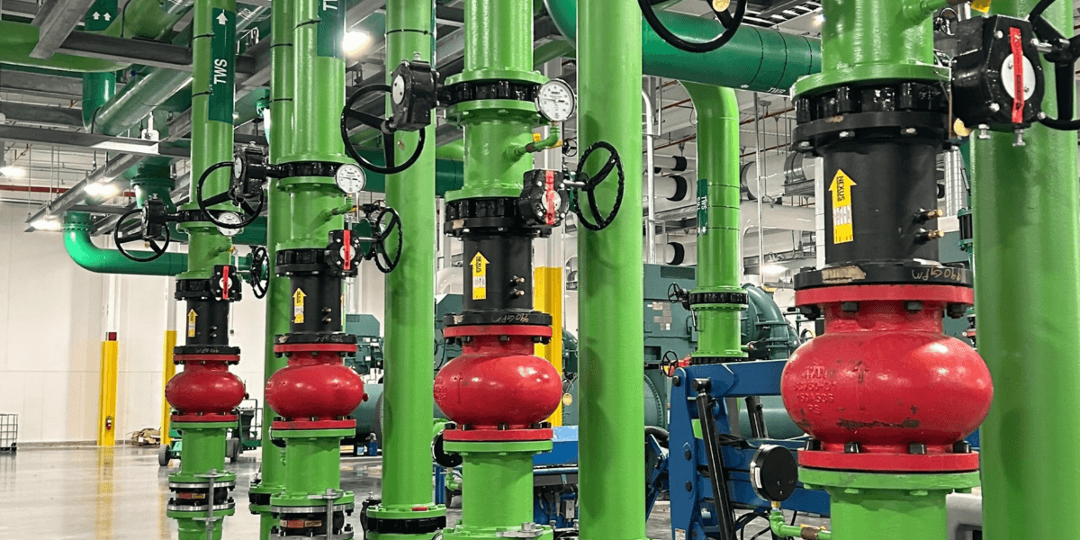 Industrial piping system with bright green pipes, red valves, and gauges inside a facility, showcasing precision fabrication and installation.