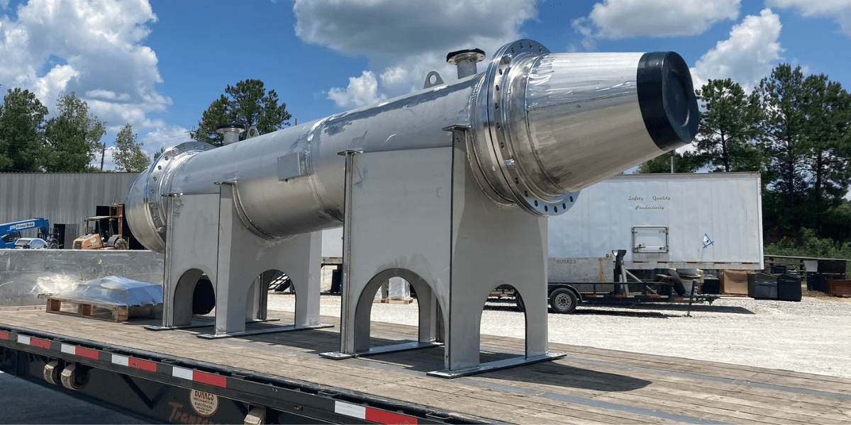 Large stainless steel industrial vessel mounted on a flatbed trailer, ready for transport from a fabrication facility.