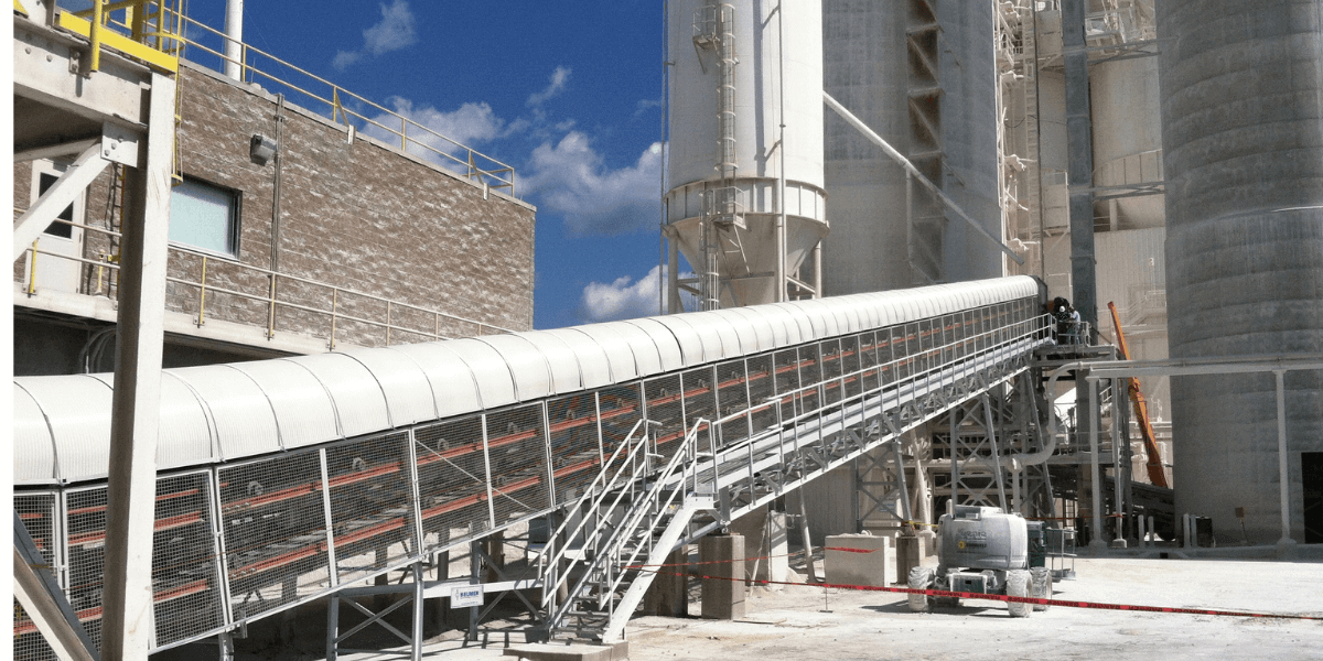 Covered industrial conveyor system with stair access installed at a cement plant facility, used for material handling and processing.