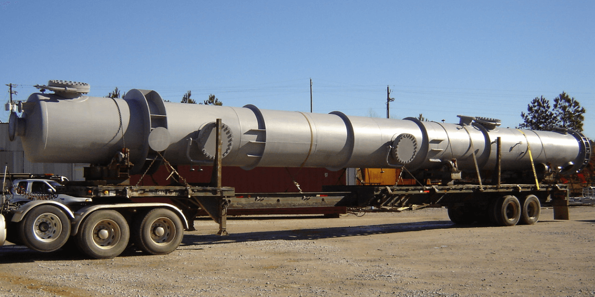 Large industrial pressure vessel loaded on a flatbed trailer for transport from a fabrication facility.