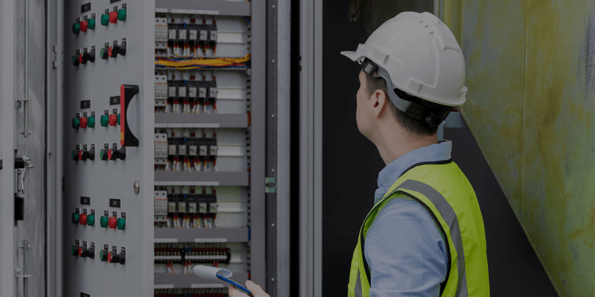 Industrial technician in hard hat inspecting electrical control panel for instrumentation calibration and system performance, representing Burkes instrumentation services.