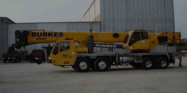 Burkes Mechanical Grove mobile crane rental (large yellow hydraulic truck crane available for heavy lifting services) parked in front of an industrial facility