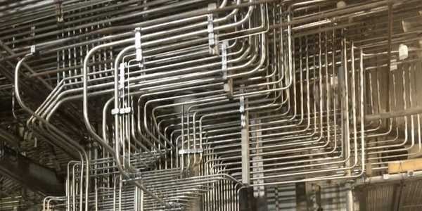 Burkes Mechanical instrumentation services stainless steel tubing installation showing precisely bent and routed instrument tubing bundles with support brackets running overhead inside an industrial plant