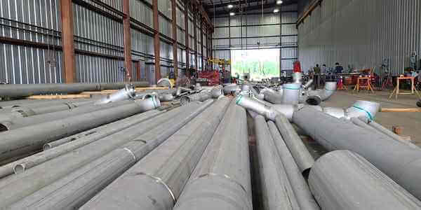 Burkes Mechanical fabrication shop interior with large-diameter stainless steel pipes and fittings staged on the floor, with welders and equipment visible in the background
